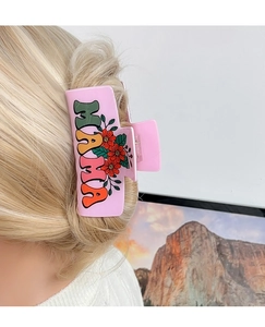 Pink MAMA hair claw clip with floral patterns holding blonde hair in a low bun