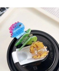 Detail view of mini acrylic dinosaur hair clips in blue, green, and orange colors