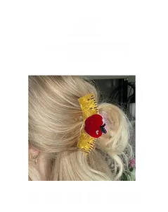 Detail view of yellow translucent ruler-shaped hair claw with a red sequin apple charm