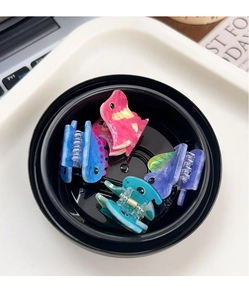 Close-up of four colorful dinosaur acrylic hair clips set in a black dish for styling