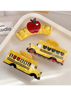Close-up of three-piece school themed hair claws with apple and bus designs on a plate