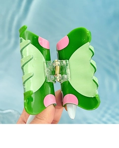 Gros plan d'une pince à cheveux en acrylique vert avec pois roses et ressort transparent