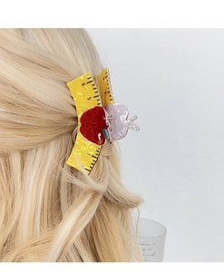 Close-up of yellow tape measure hair claw with red apple design on blonde hair