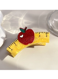 Detail view of a yellow acetate hair claw clip with ruler marks and a red glitter apple