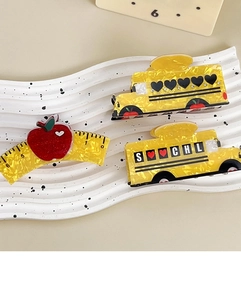Detail view of yellow school bus and ruler hair claws with rhinestones on a white tray
