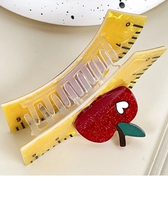 Macro detail of yellow ruler hair claw clip with red apple and glitter heart accent