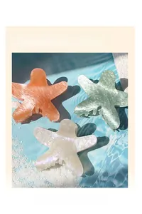 Close-up of glittery starfish hair claws in coral pink and mint green on beach background