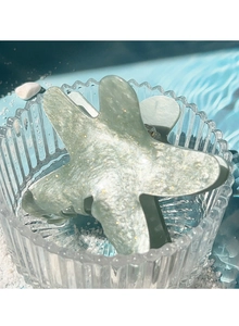 Detail of glitter starfish hair claw clip on white sand with ocean beach aesthetic