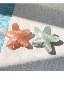 Detail of two starfish hair claws in pearlescent orange and mint green on stone