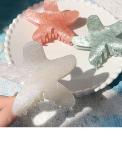 Detail of colorful starfish hair claws with glitter texture on a beach-themed background