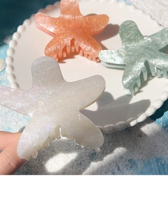 Detail of colorful starfish hair claws with glitter finish on beach sand tray