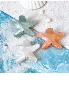 Macro detail of three starfish hair claws in pastel marble colors on a beach background
