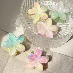 Iridescent frangipani flower hair claws in pastel colors displayed on linen fabric