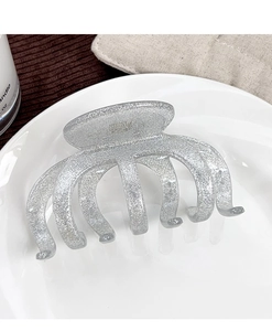 Close-up of a silver glitter hair claw clip with a transparent texture on a ceramic plate
