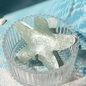 Sparkly light green starfish hair claw clip with pearlescent finish on a beach setting