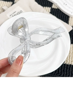 Close-up of sparkling silver bow hair claw clip with fine glitter held in hand