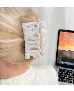 Gros plan sur une pince à cheveux marbrée avec lettrage Bride en perles blanches