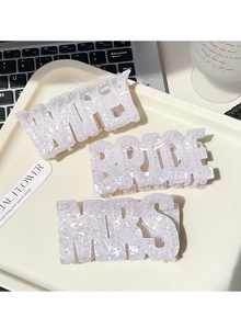 Détail des pinces à cheveux crème avec lettrage en perles WIFEY BRIDE MRS sur plateau