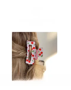 Detail of a white cherry print rectangular hair claw clip worn on wavy brown hair