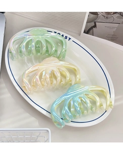 Macro shot of large iridescent claw clips in pastel colors on a stylish ceramic plate