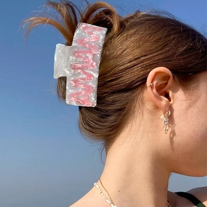 Elegant marble white hair claw clip with pink letters worn on model hair against blue sky