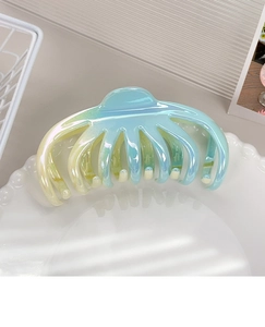 Close-up of a large iridescent gradient hair claw clip on a decorative ceramic dish