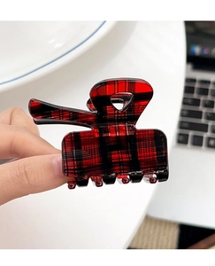 Detailed close-up of a red and black plaid acetate hair claw clip held in hand for hair styling