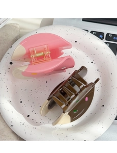 Detail of pink and brown acetate hair claws with gold springs in a ceramic tray