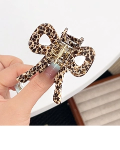 Close-up of leopard print bow hair claw clip with golden metal spring and acrylic texture