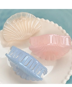 Three jelly-colored shell hair claws in beige, pink, and blue on a white ceramic plate