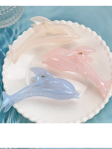 Three jelly-colored dolphin hair claws in cream, pink, and blue on a vintage pearl plate