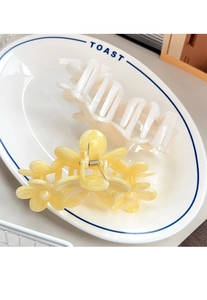 Close-up of floral hair claw clips in yellow and white resin on a white plate
