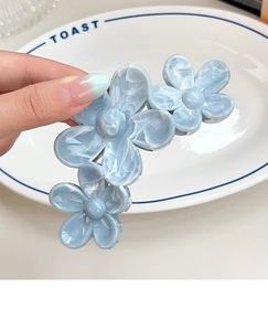 Detail of light blue floral hair claw clip with marble texture held over a ceramic dish