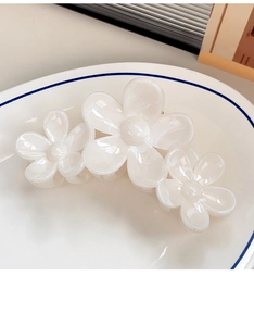 Detailed macro view of a large white floral hair claw clip in an elegant ceramic dish