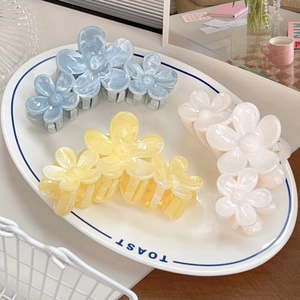 Floral hair claw set in light blue, yellow, and white colors on a white ceramic plate