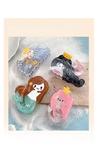 Detail of four colorful mermaid-shaped acetate hair claw clips on white sand with shells