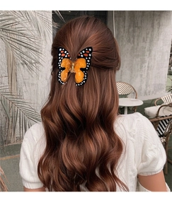 Détail d'une pince à cheveux papillon en résine orange sur de longs cheveux bouclés