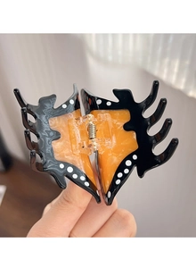 Détail d'une pince à cheveux papillon avec motifs ambrés orange et pois blancs sur acétate