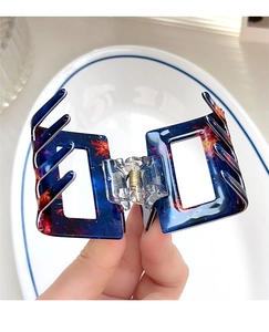 Detail of a rectangular hair claw clip with a blue nebula art pattern held by hand