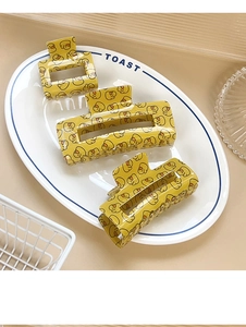 Detailed set of three yellow hair claws with duck pattern on a decorative ceramic plate