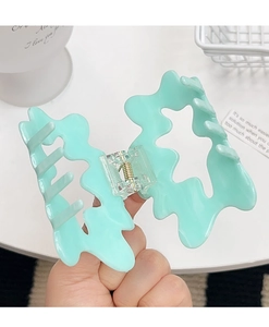 Detail showing mint green wave-shaped hair claw clip with glossy finish and metal spring