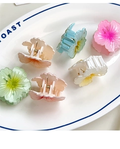 Detailed view of six small colorful macaron plumeria flower claw clips in a white plate