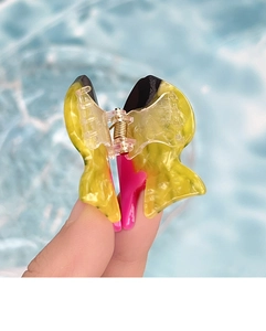 Detailed close-up of a small yellow acetate fish hair clip with marble pattern and metal spring
