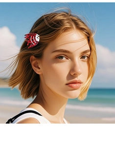 Red fish-shaped hair clip with spots on blonde hair against a sunny beach background