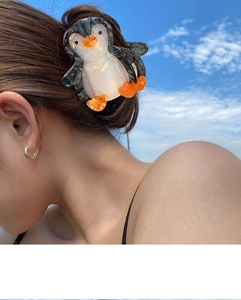 Detail showing marble texture penguin hair claw clip worn on hair with blue sky background