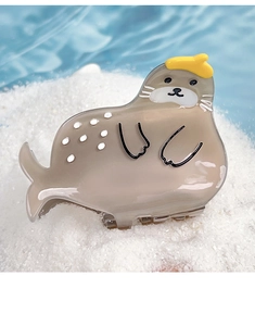 Detailed view of grey acetate seal hair claw clip with yellow hat on a beach sand background