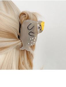 Detail of grey acetate cartoon seal hair claw clip worn on blonde hair in macro view