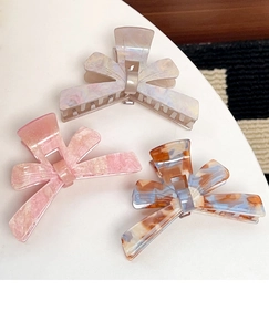 Detailed close-up of bow hair claws in marble, tortoiseshell, and pearlescent finishes