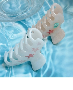 Détail de pinces à cheveux étoiles de mer en blanc et givré sur fond de vagues d'eau bleues