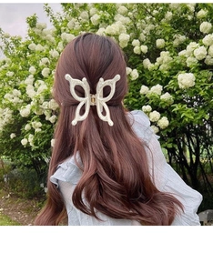 Close-up of cream butterfly hair claw clip with pearl accents on brown wavy hair
